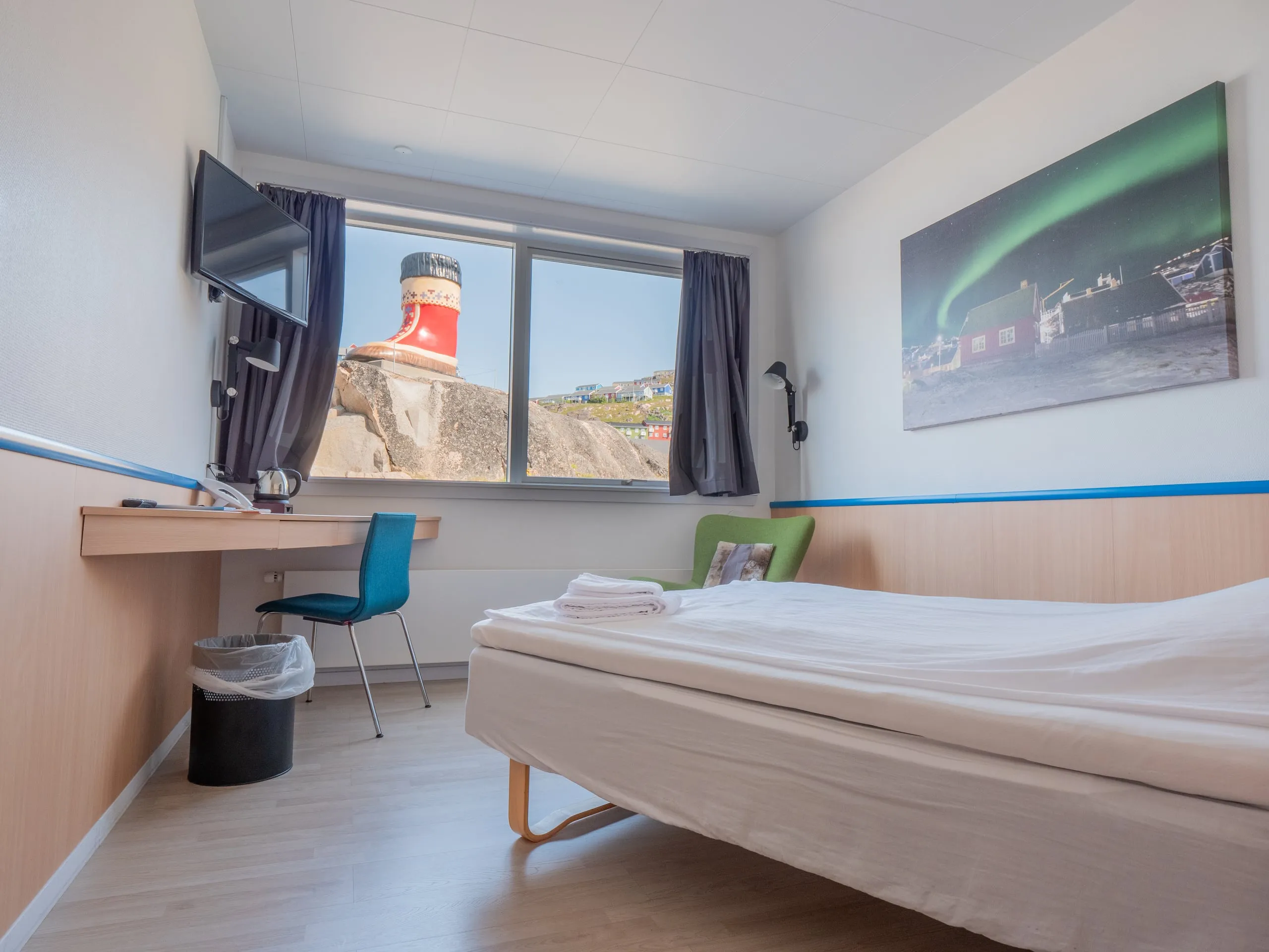 A single room: the bed along the wall, a desk under the TV, and a window over the harbour, beneath a picture of the northern lights.