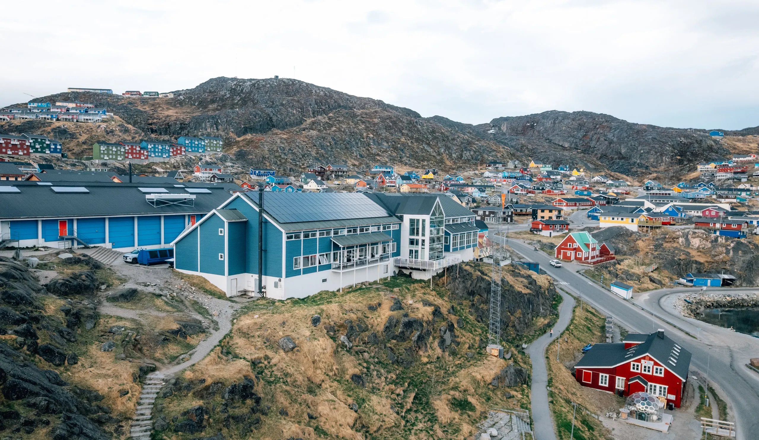 Hotel Qaqortoq from above: the long blue hotel on the rocks, with the coloured houses of the town on the hills behind.