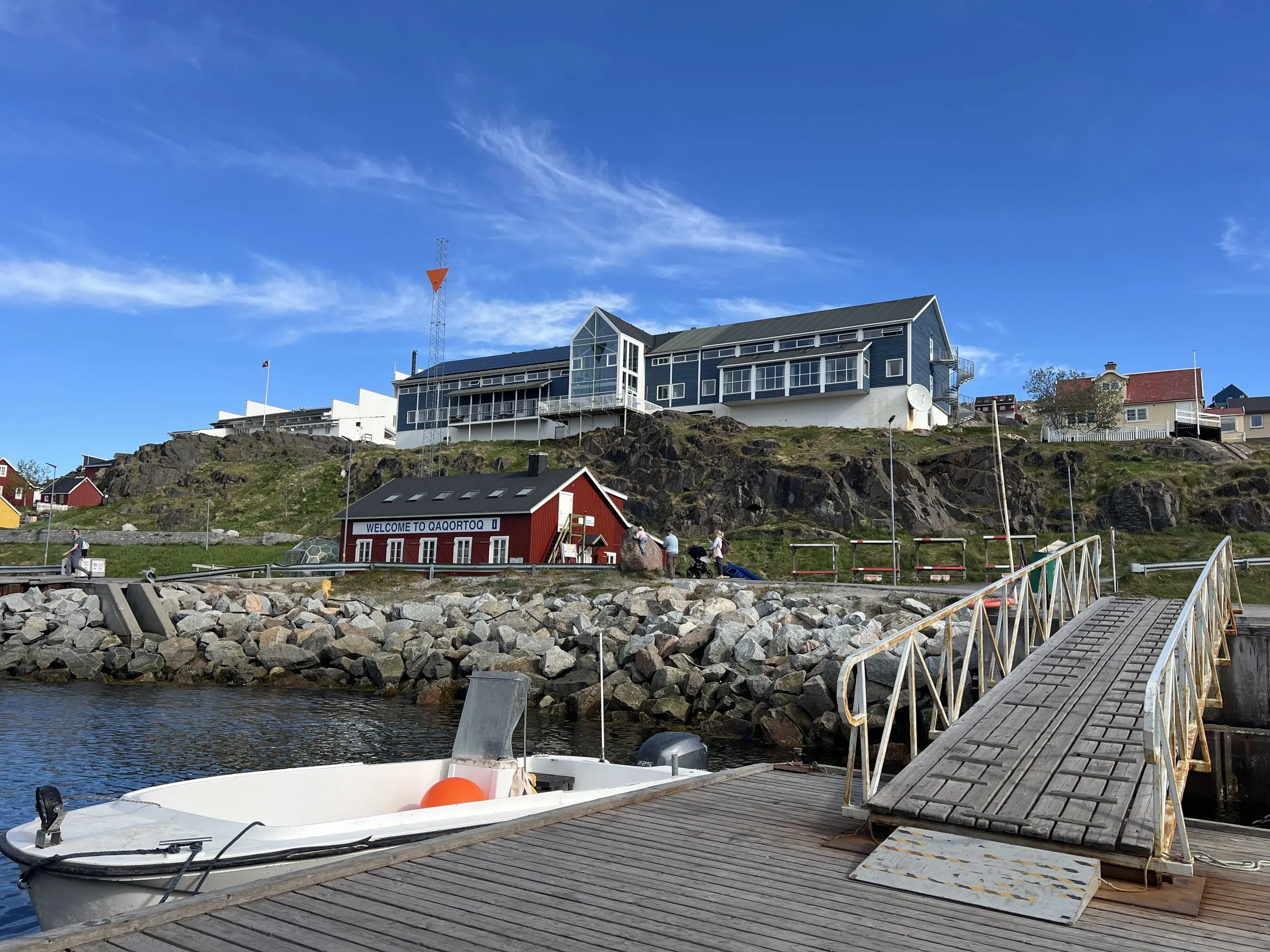 The hotel on the hill above the harbour, seen from a jetty with a small boat moored below.