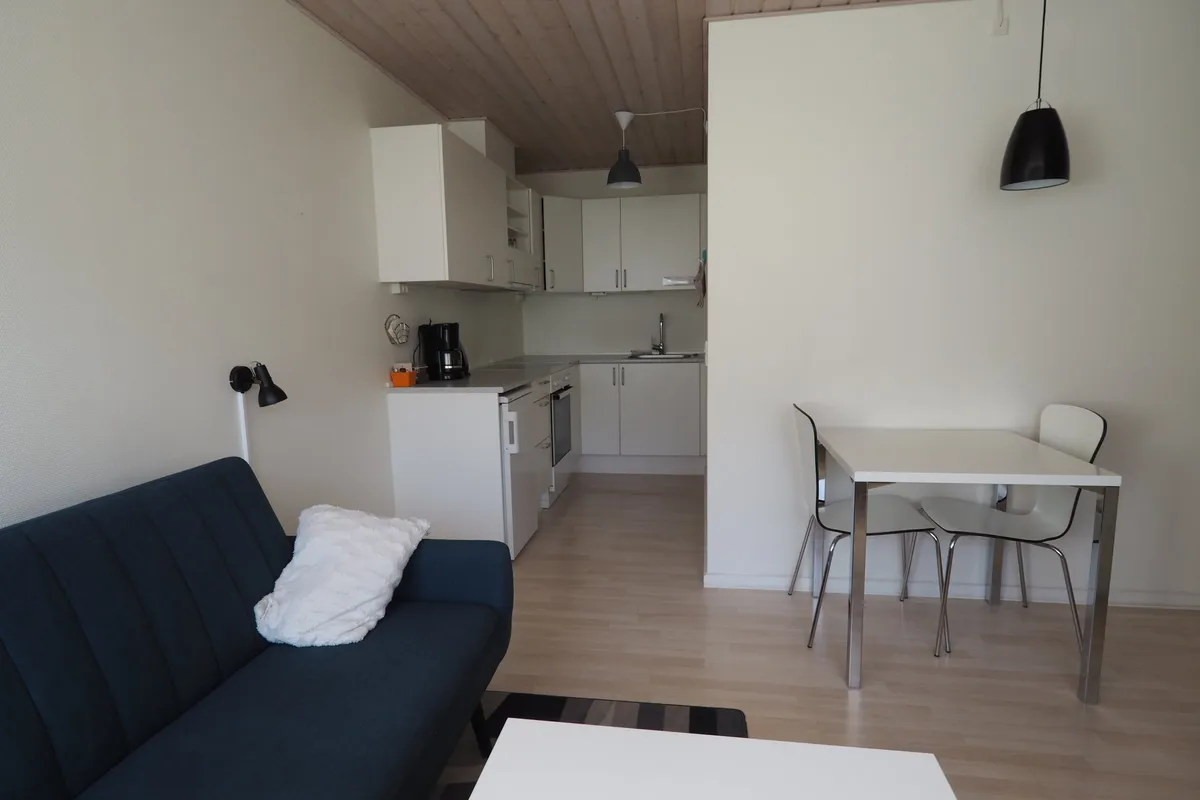 An apartment living room with a blue sofa and a dining table, looking towards the kitchen.