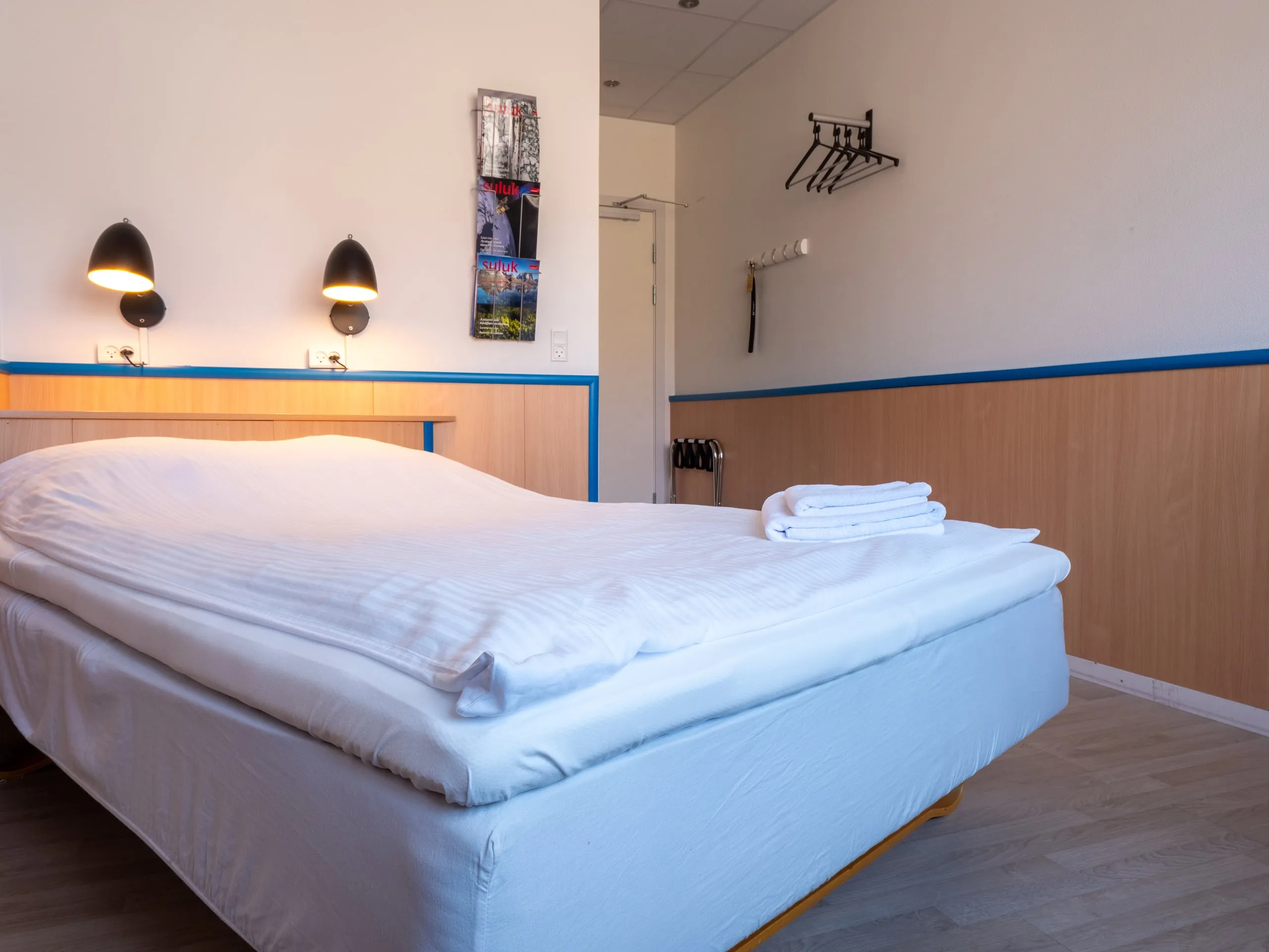 The full bed in a single room, made up with white linen and towels, with two reading lamps above it.
