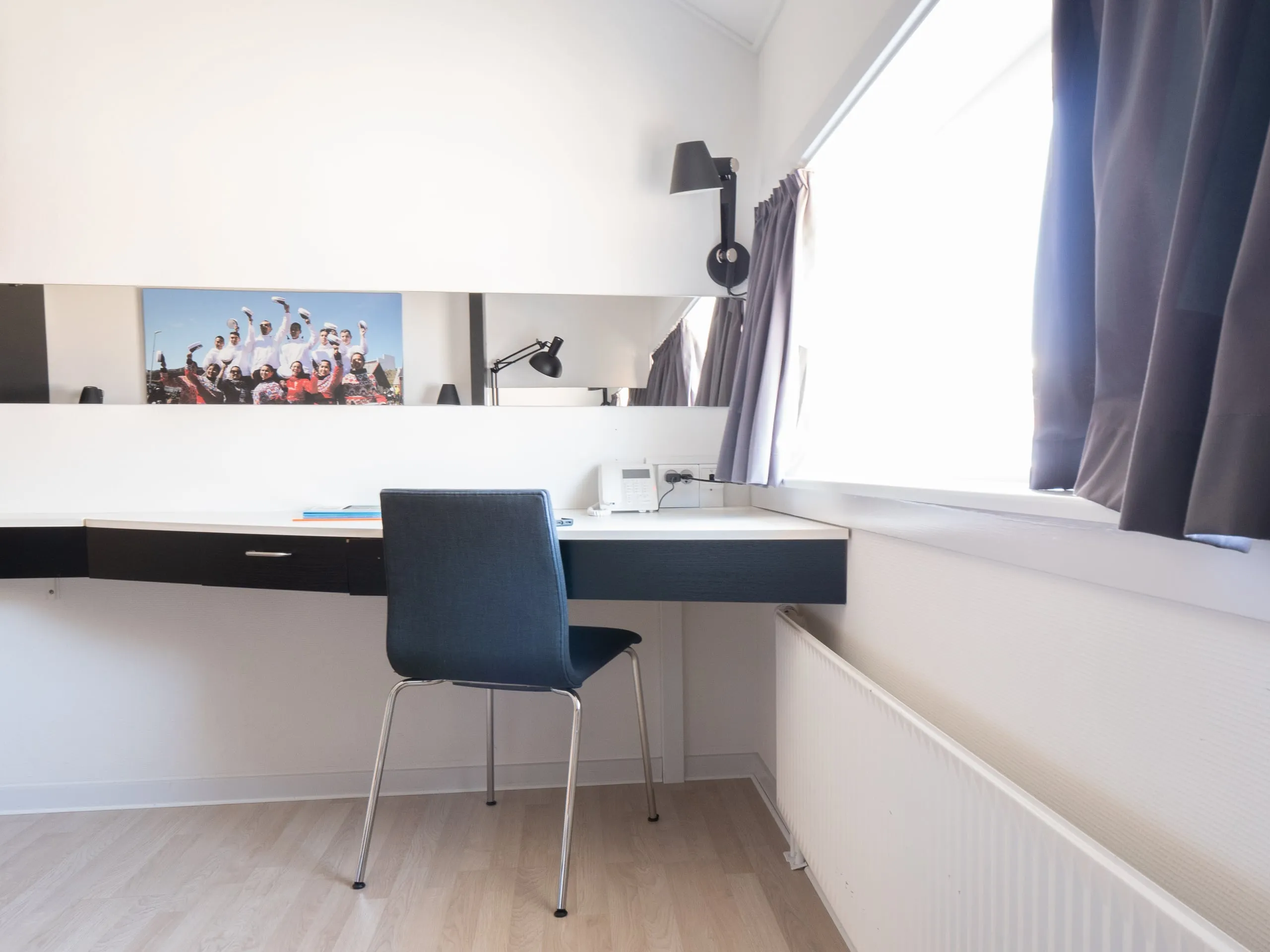 The desk in a double room, beneath a photograph and beside a tall window.