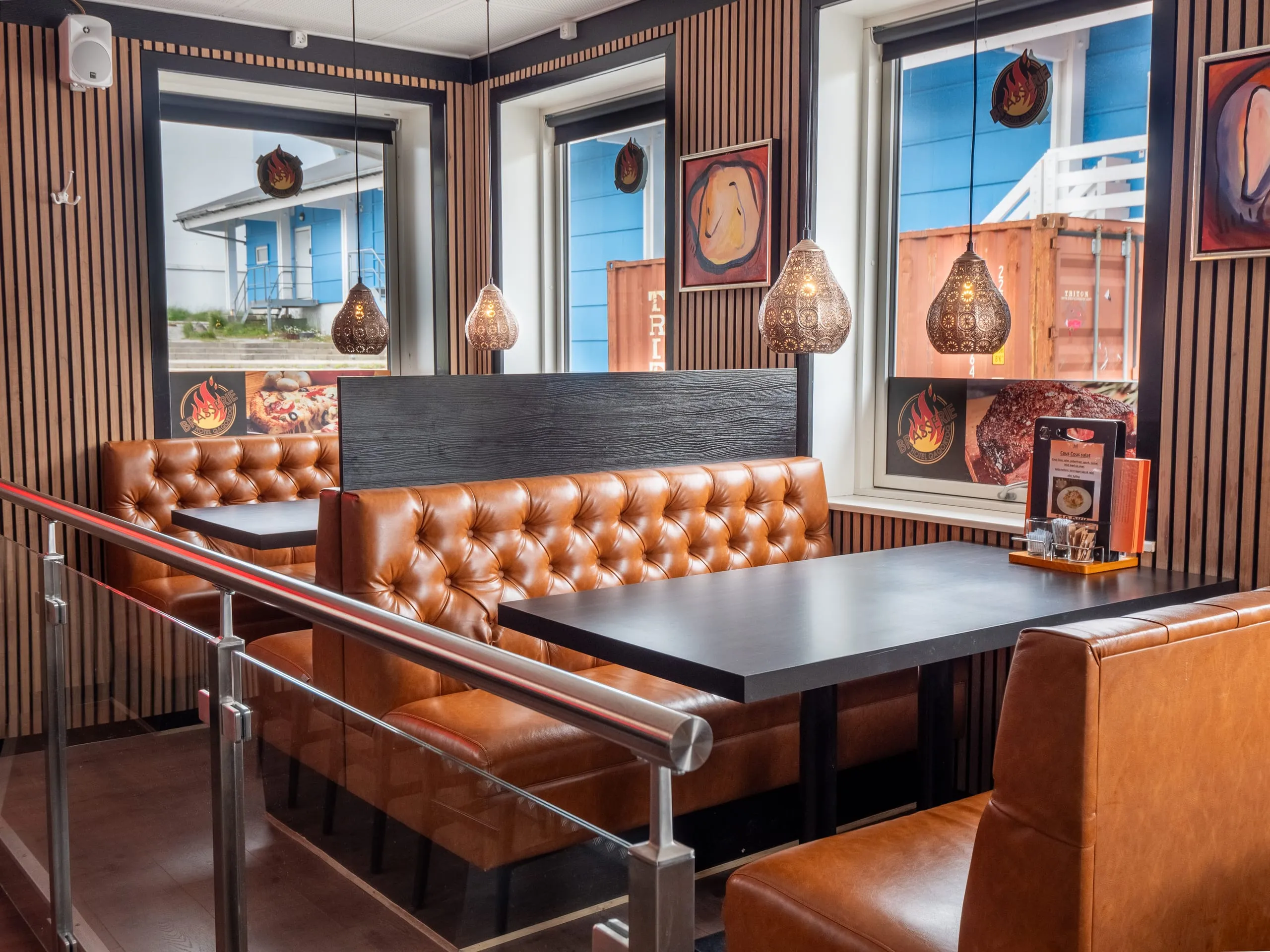 Tufted leather booths under pierced copper lamps, by windows looking out on a blue house next door.