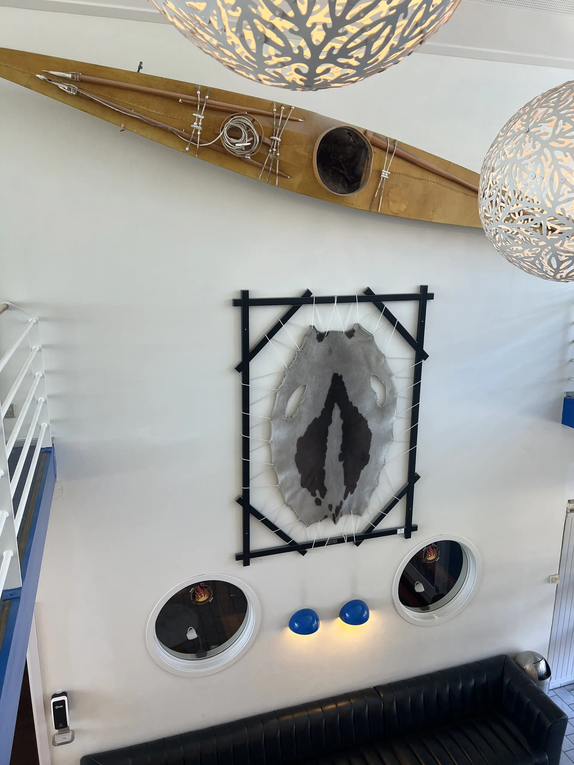 A kayak and a framed Greenlandic artwork on a white wall, under patterned pendant lamps.