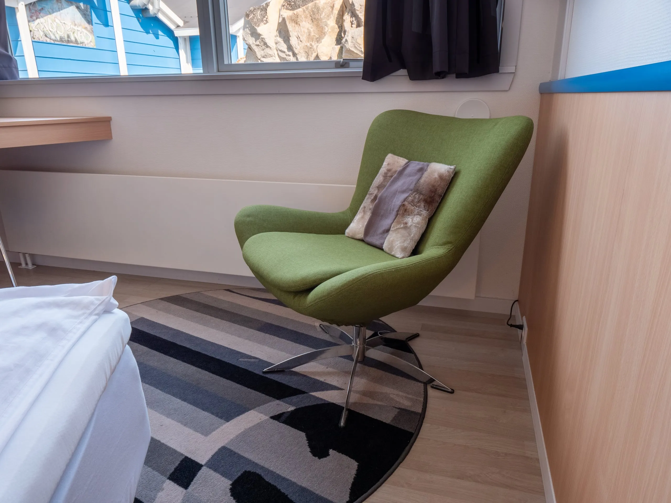 A green armchair with a cushion on a patterned rug by the window of a single room.