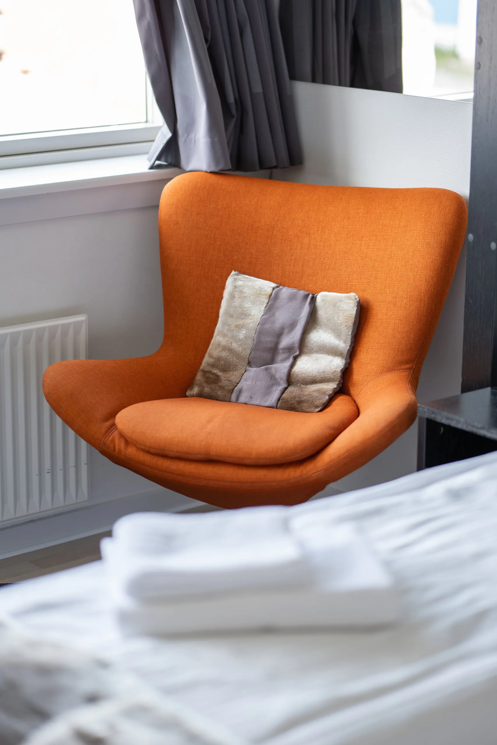 An orange armchair with a cushion by the window of a double room.