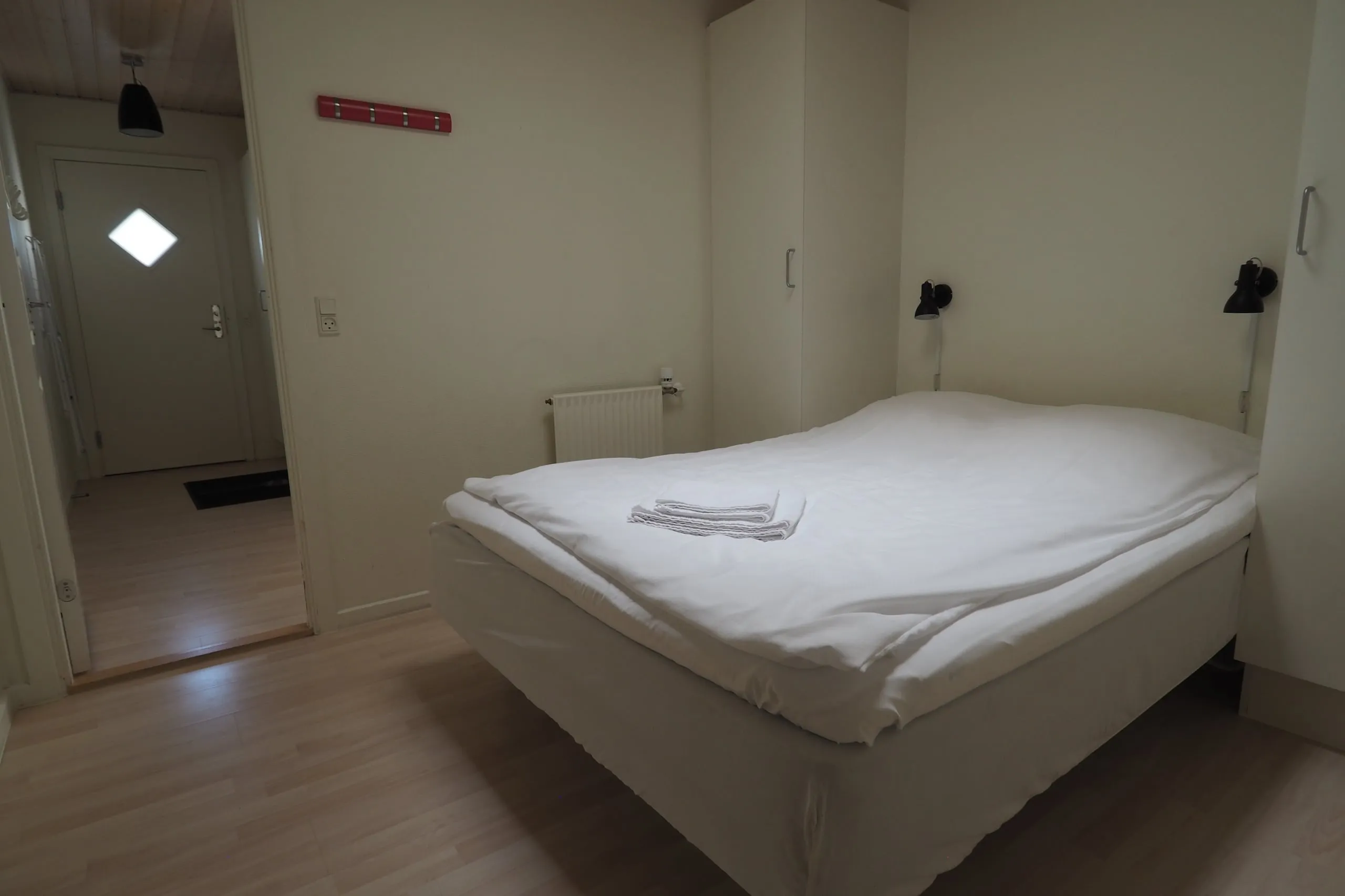 An apartment bedroom with a made-up bed and a reading lamp on the wall.