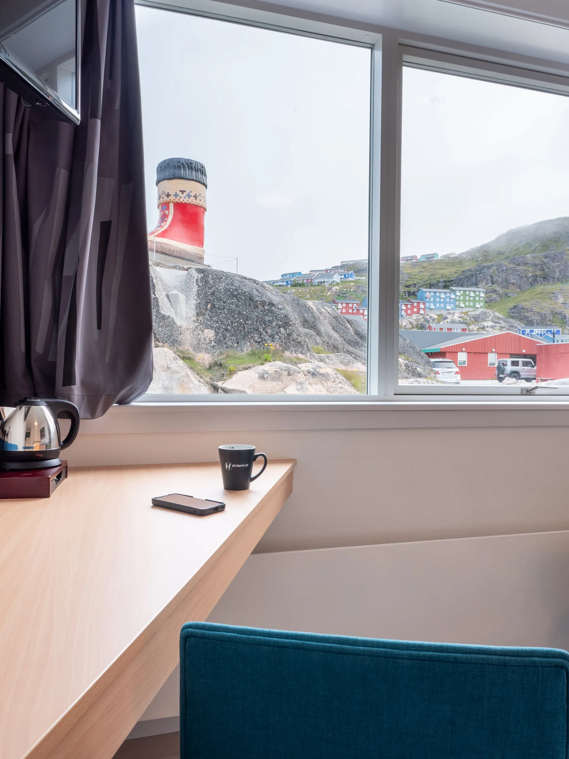 The desk at the window of a single room, with a kettle and a mug, looking out over the harbour.