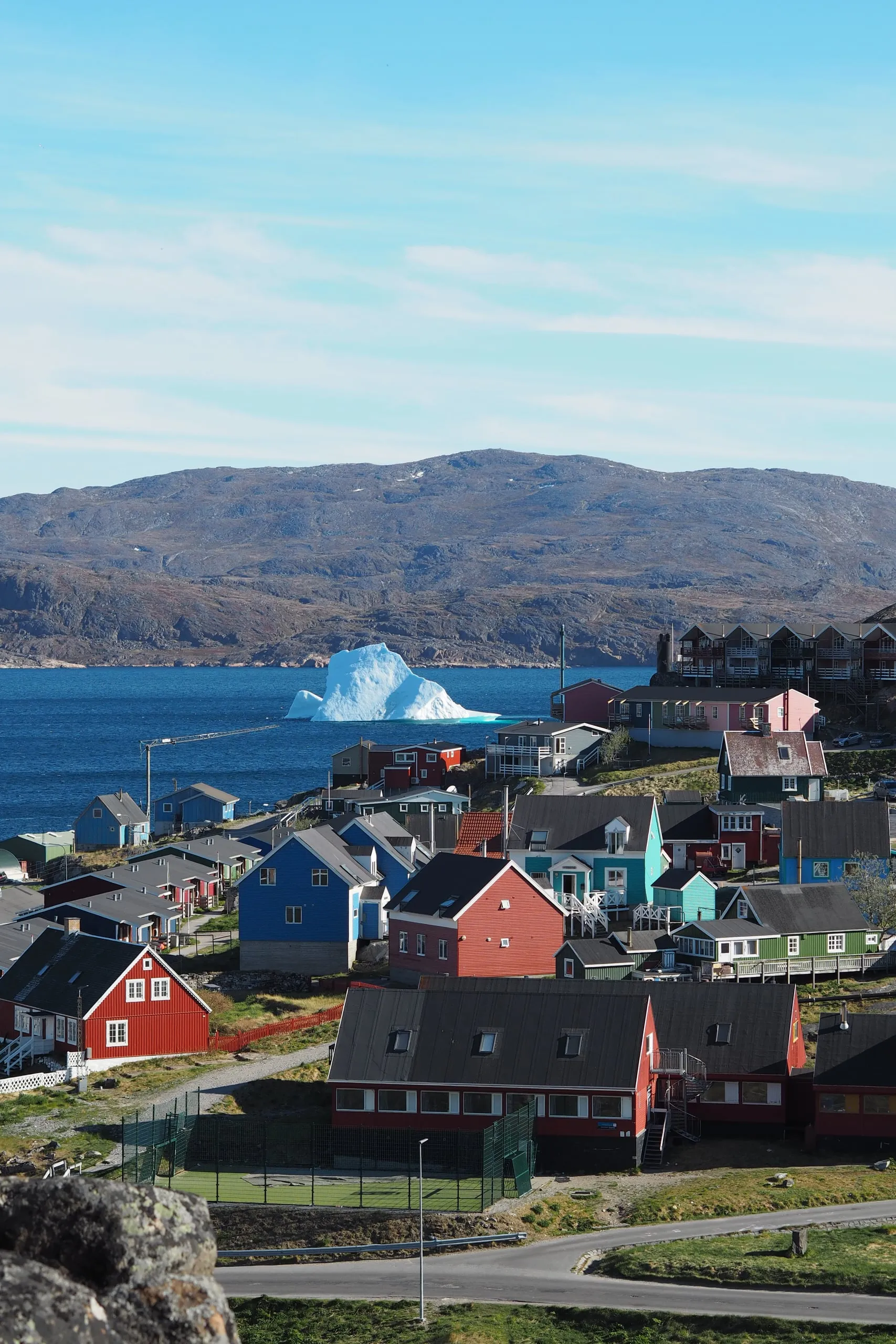 Coloured houses stepping down to the harbour, with an iceberg in the fjord and hills behind.