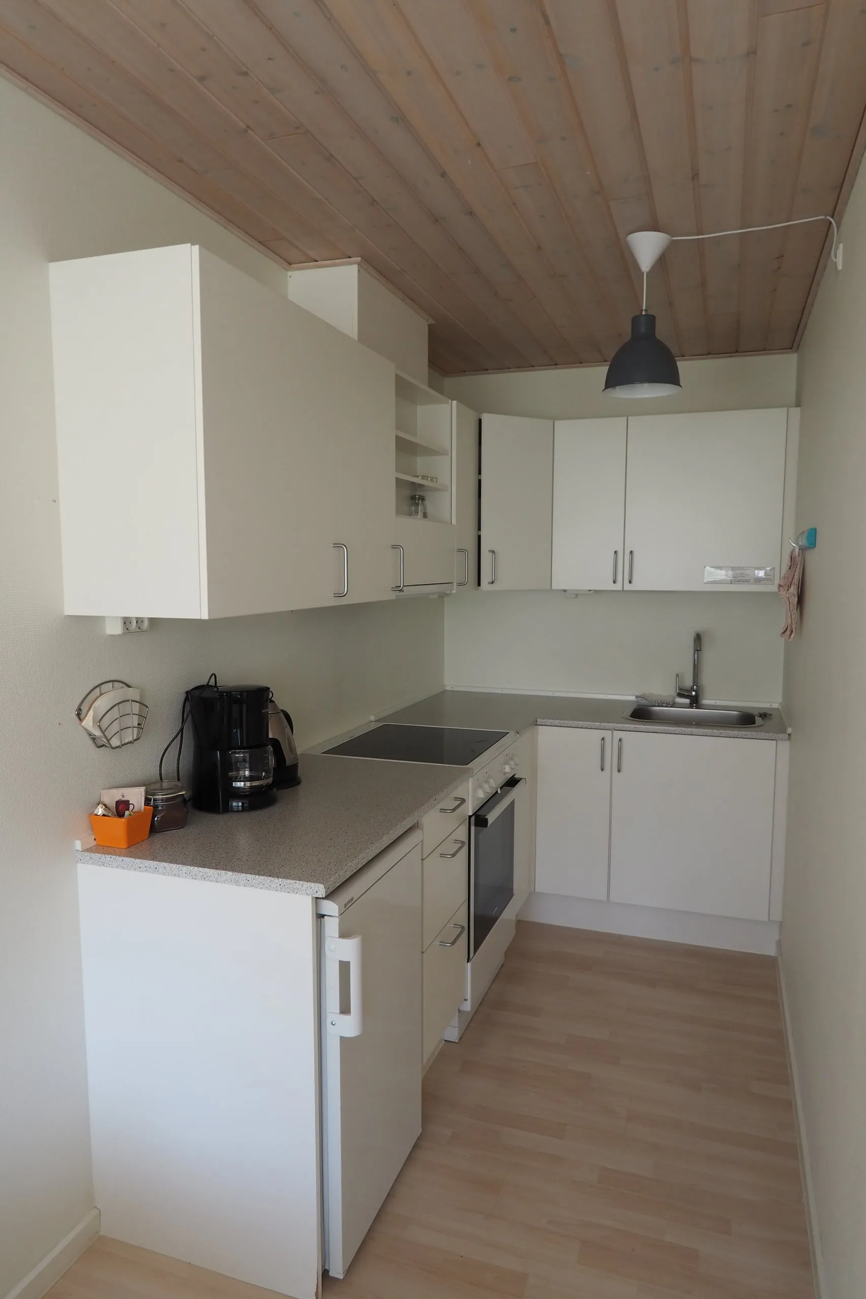 The length of an apartment kitchen, with white cupboards, a coffee maker and an oven.