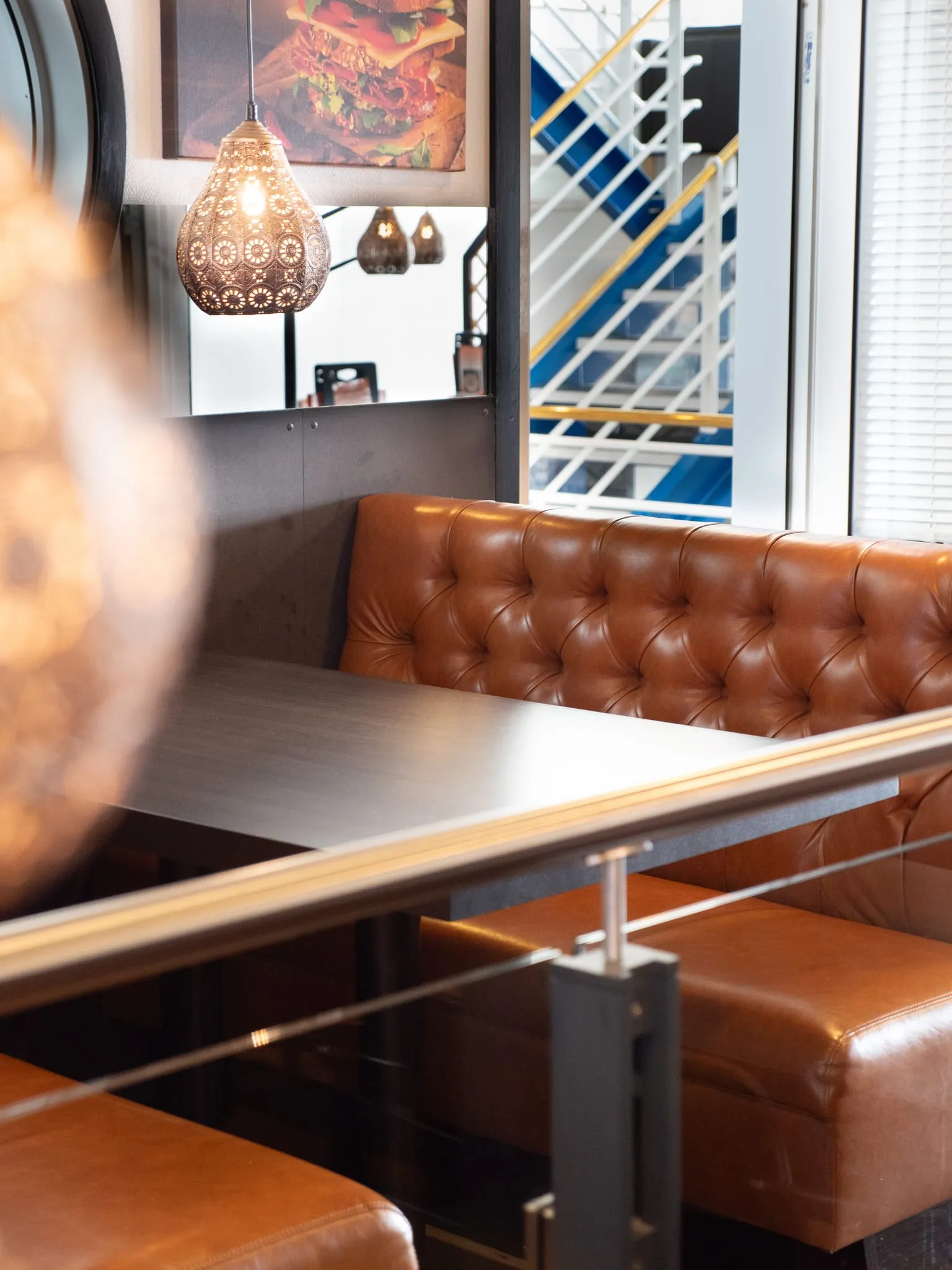 A leather booth and table beside the glass rail of the stairs, under a copper lamp.