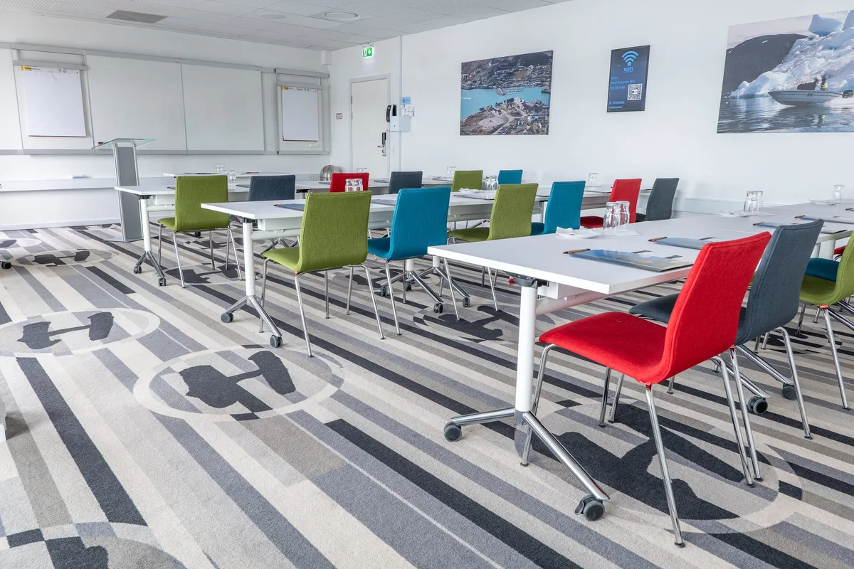 Tables and green, blue and red chairs set out in a conference room hung with photographs of Greenland.