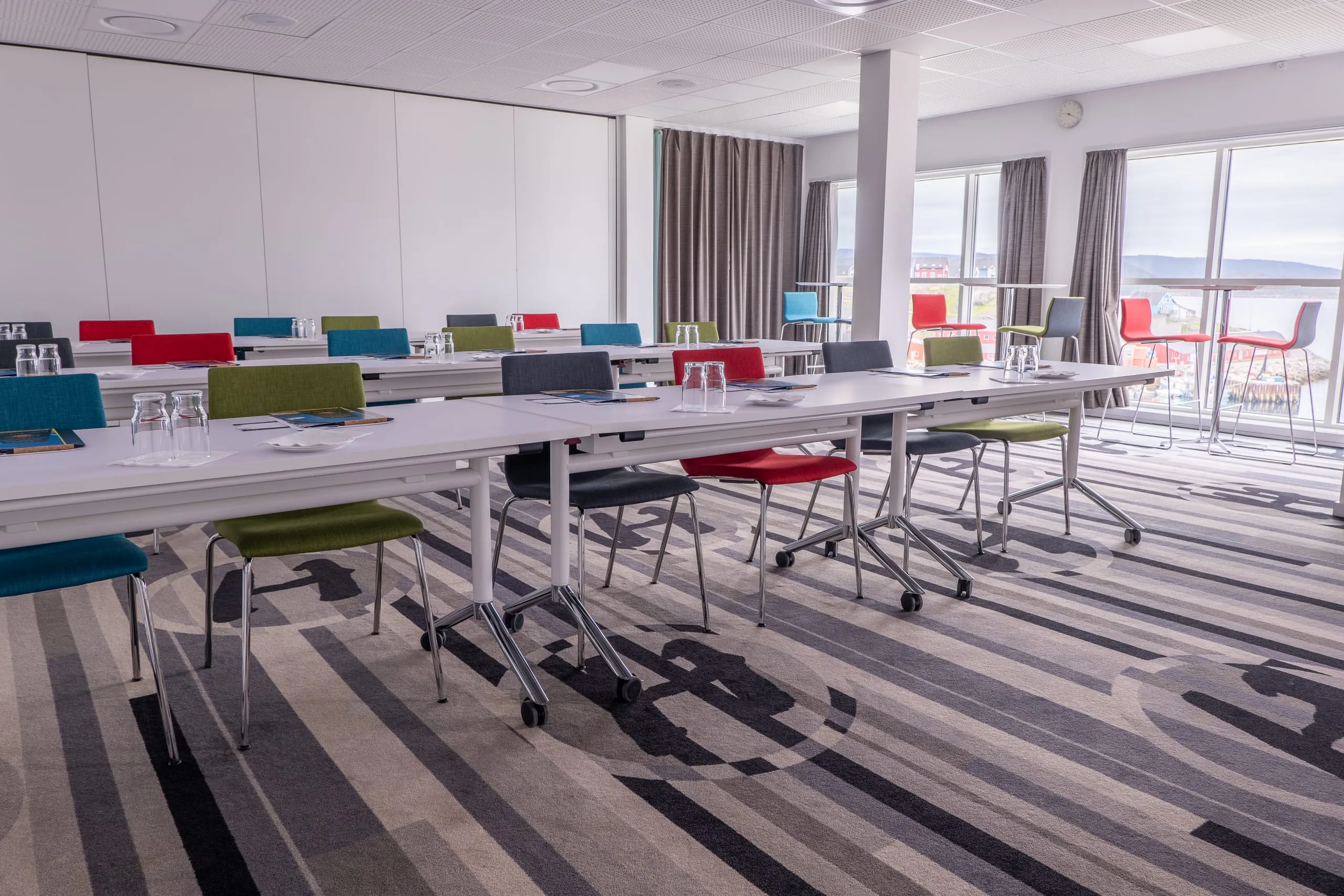 The conference venue set with rows of tables and colourful chairs, its tall windows looking out over Qaqortoq.