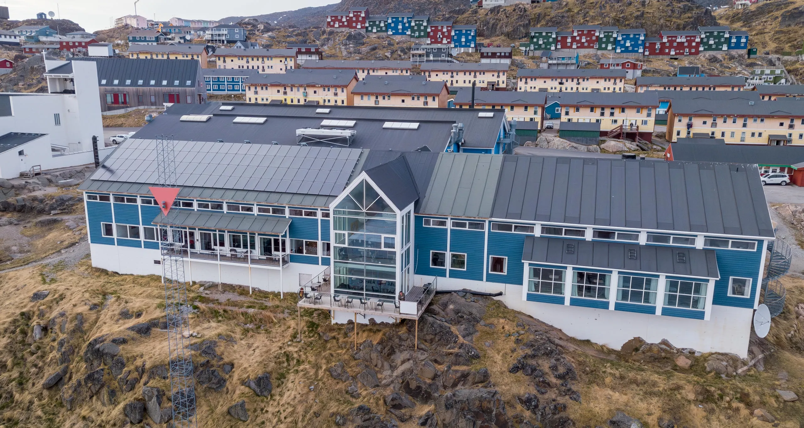 Hotel Qaqortoq from above: the blue timber hotel on the rocks, with the colourful houses of Qaqortoq behind it.