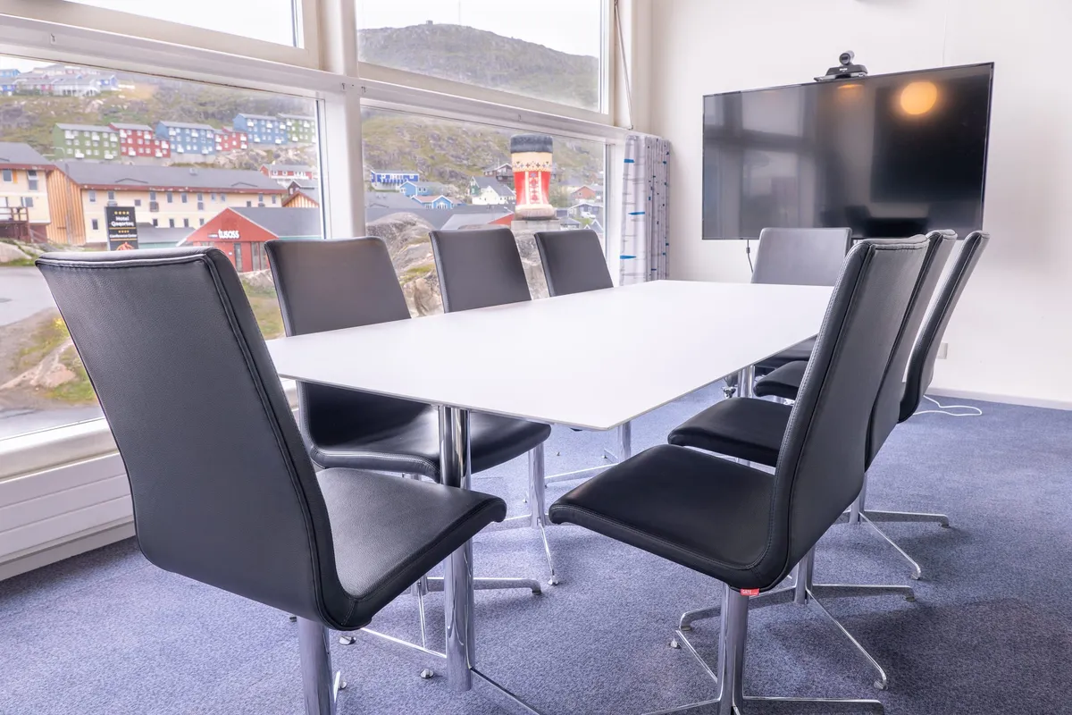 A meeting room with black leather chairs around a white table, a screen on the wall and the town outside.